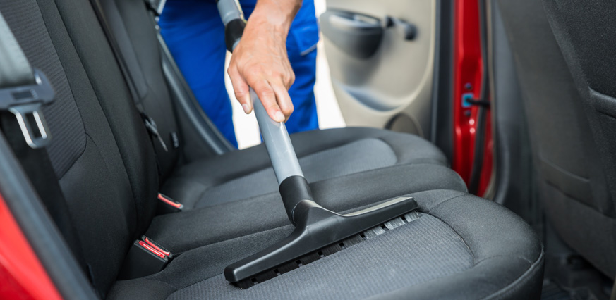 A person using a vacuum to clean the seat of a car.
